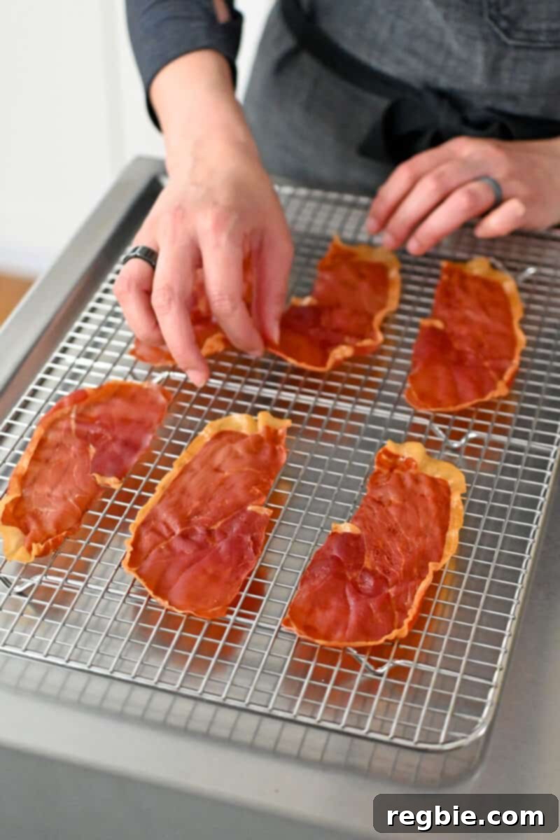 Golden Prosciutto Snaps 7 A hand is placing crispy prosciutto chips on a cooling rack