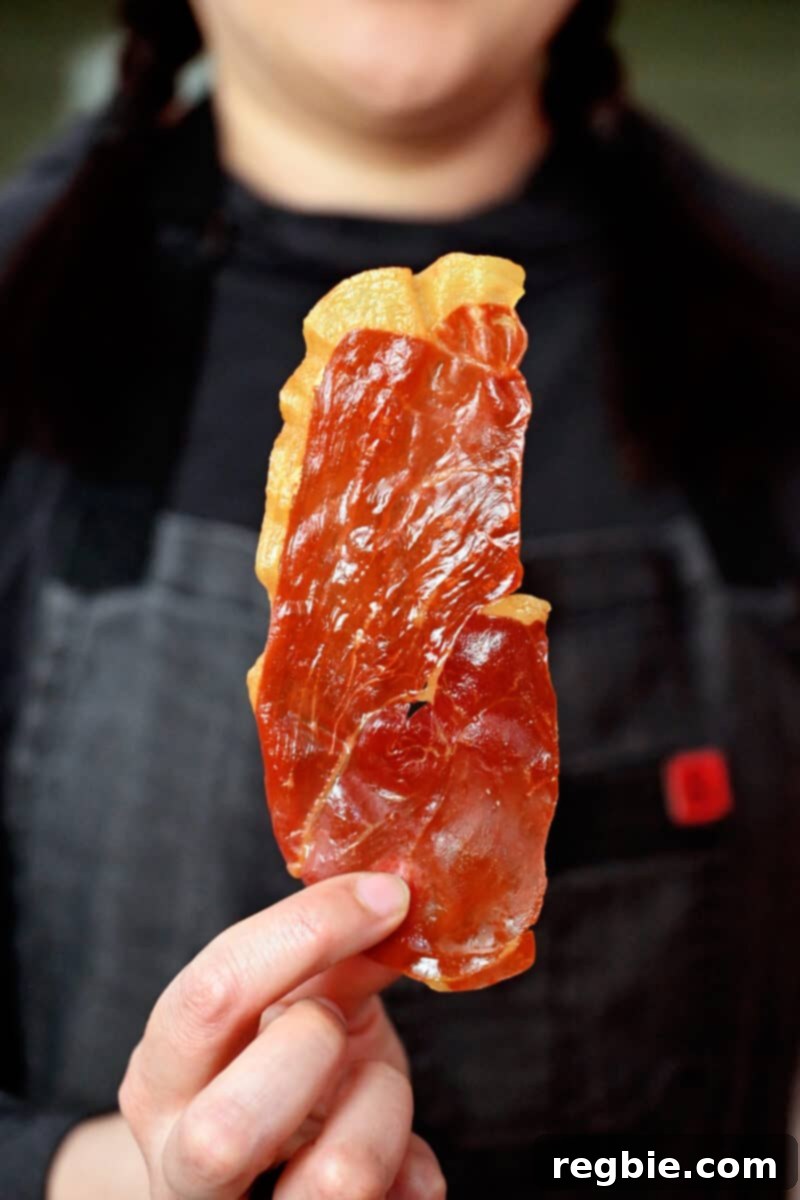 Golden Prosciutto Snaps 8 A person in a gray apron is holding up a crispy prosciutto chip