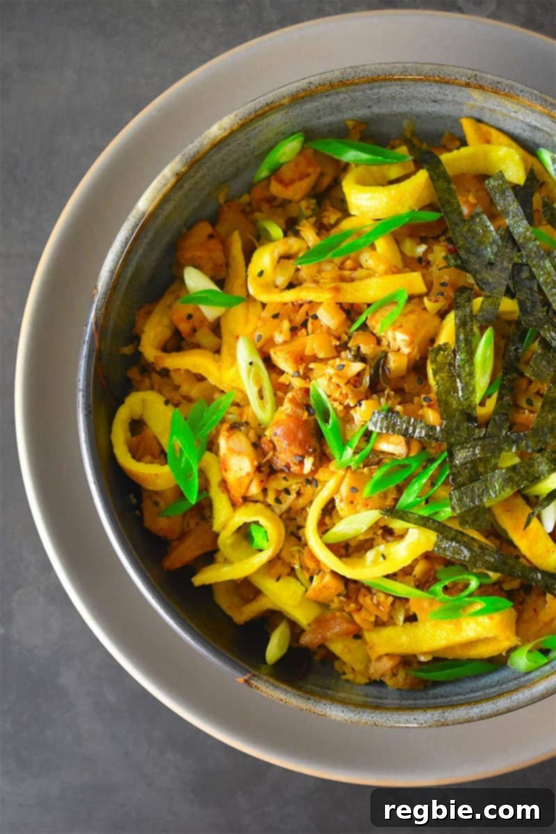 An overhead shot of a steaming bowl of Kimchi Cauliflower Fried Rice garnished with scallions and nori, highlighting its vibrant colors and inviting texture.