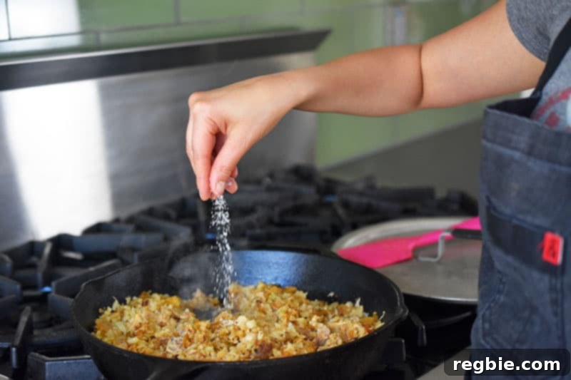 A hand sprinkling kosher salt into the cooked kimchi cauliflower fried rice in the pan, adjusting seasoning.