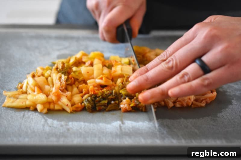 A close-up shot of hands carefully chopping vibrant red kimchi on a wooden cutting board, preparing it for the fried rice.