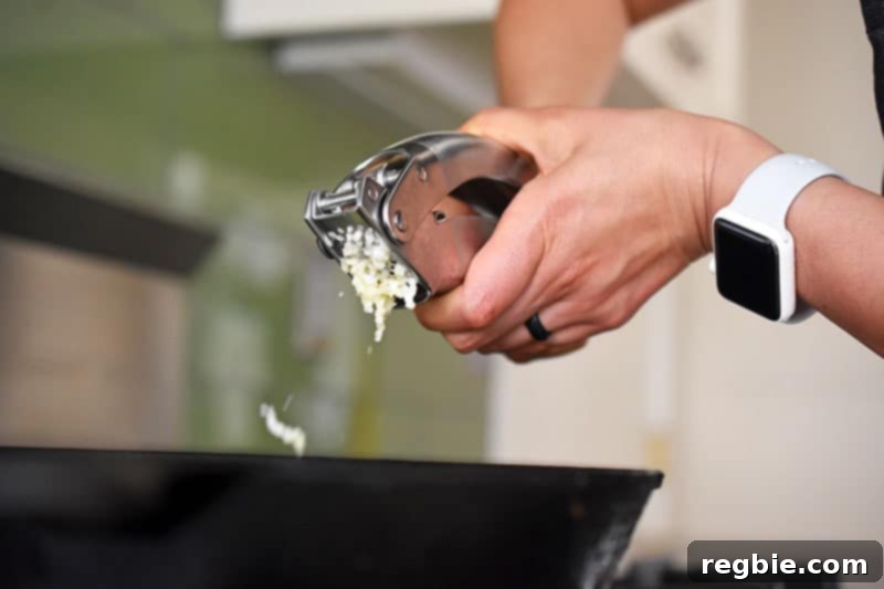 Minced garlic being added to the sautéed onions in the pan, creating a fragrant aromatic base.