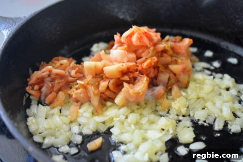 Chopped kimchi combined with sautéed onions and garlic in a hot pan, stir-frying to develop deeper flavors.