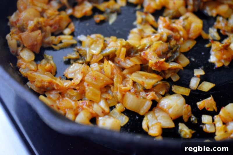 The kimchi, onions, and garlic mixture browning slightly in the pan after a few minutes of stir-frying, indicating enhanced flavor.