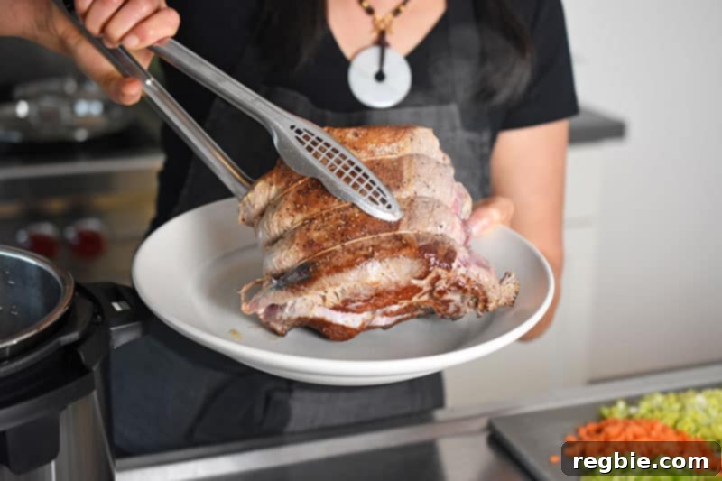 Transferring the seared chuck roast from the Instant Pot to a platter with a pair of tongs