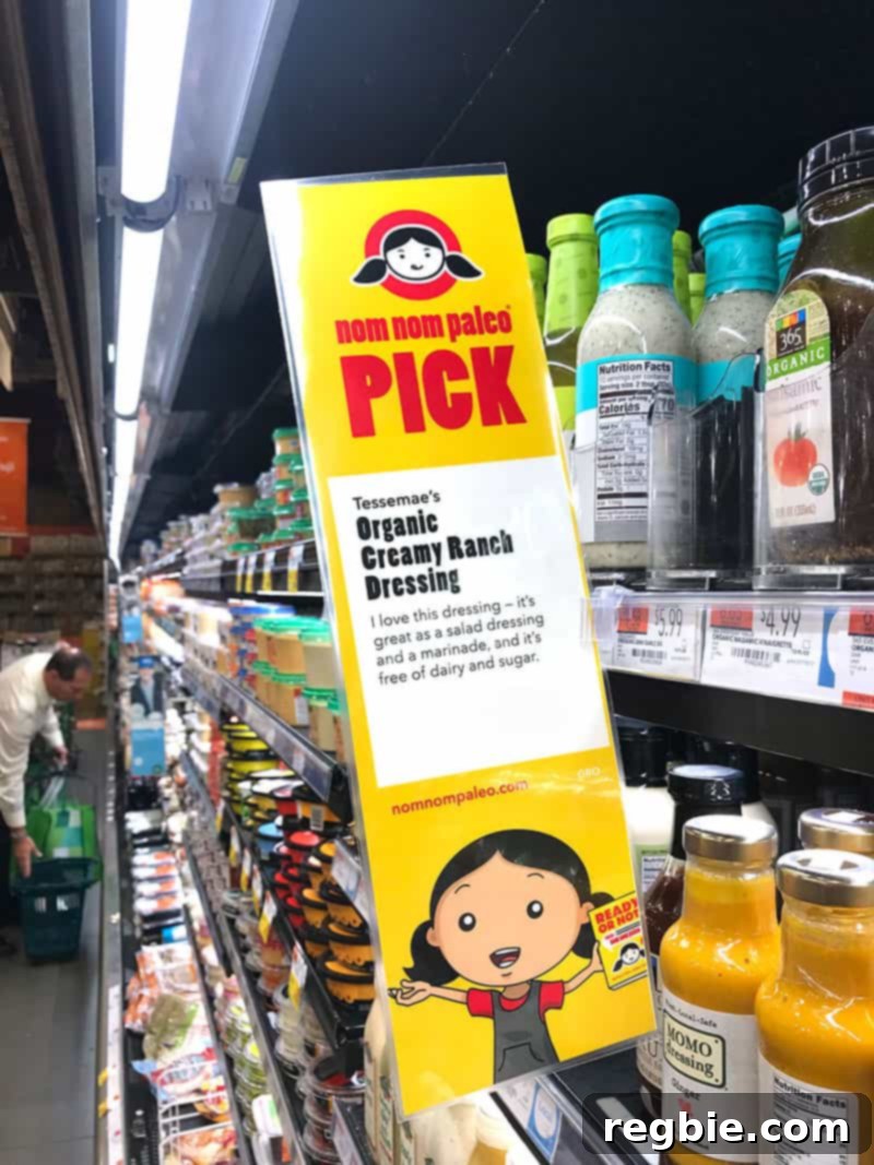 A Nom Nom Paleo Picks sign prominently displayed on a Whole Foods Market shelf, highlighting a Paleo-friendly product.