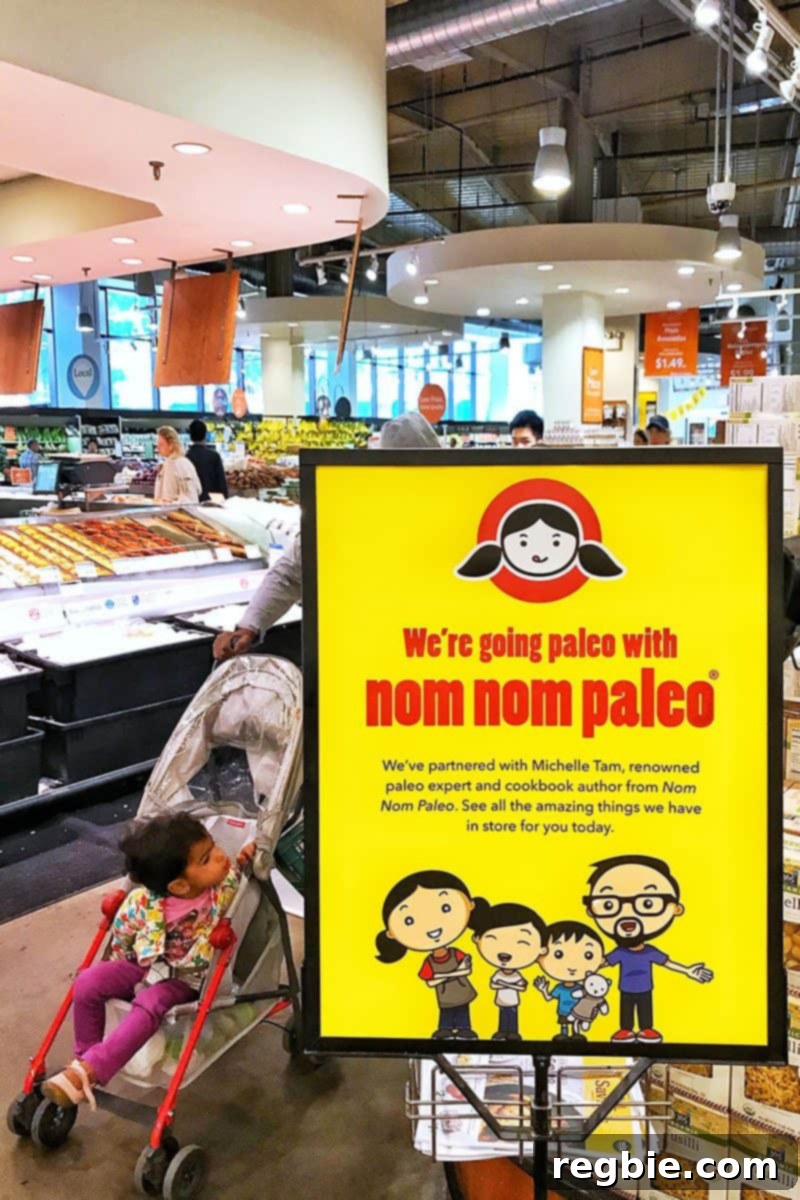 Michelle Tam, smiling, points to a Nom Nom Paleo Picks sign in the Tribeca Whole Foods Market store.
