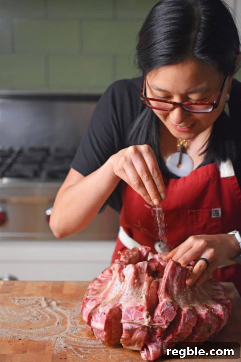 Someone seasoning Magic Crown Roast of Pork with Magic Mushroom Powder, ensuring even coverage.