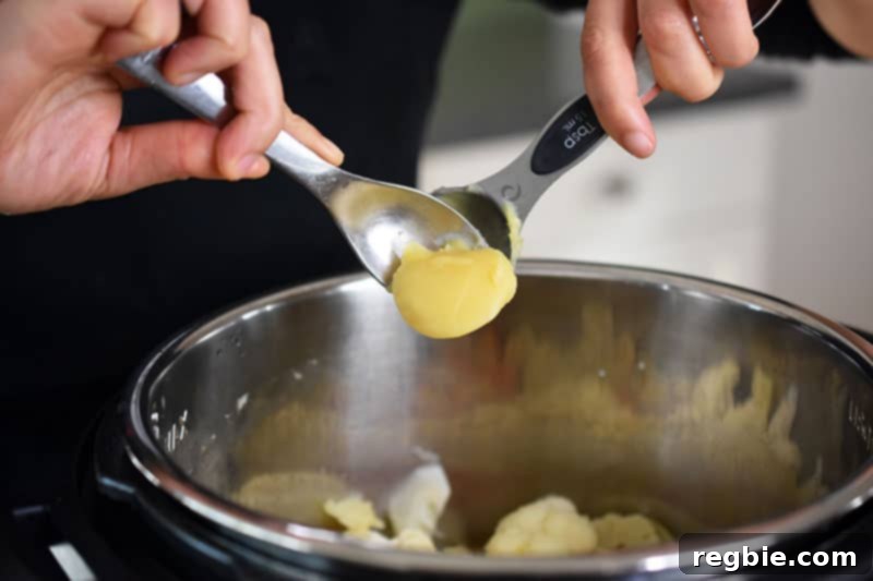 Instant Pot Wholesome Autumn Mash 13 A spoonful of ghee being added to the cooked vegetables in the Instant Pot, ready for final seasoning and blending.