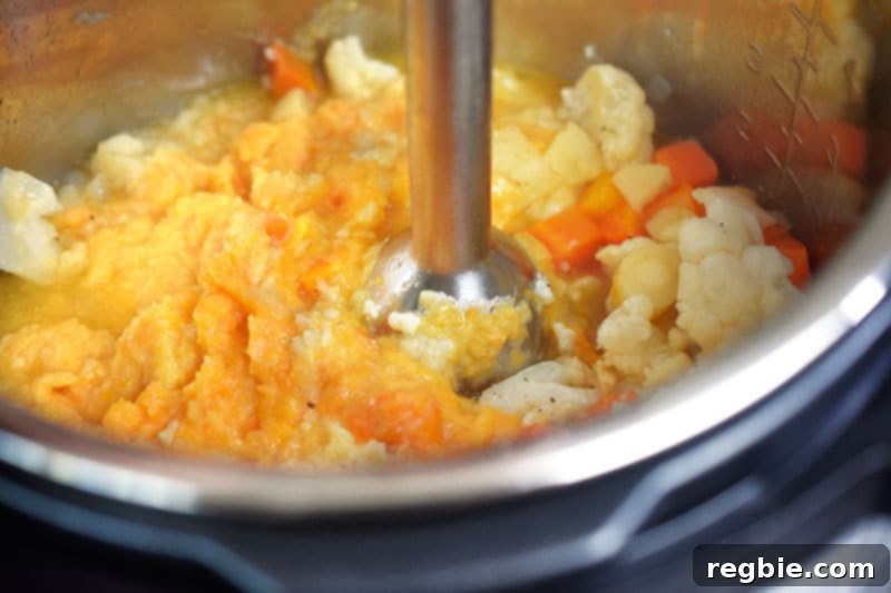 Instant Pot Wholesome Autumn Mash 14 An immersion blender actively puréeing the autumn mash mixture directly in the Instant Pot, creating a smooth and creamy texture.