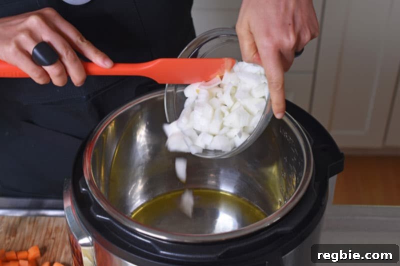 Instant Pot Wholesome Autumn Mash 6 A hand adding finely chopped onions to the hot Instant Pot with melted ghee, ready for sautéing.