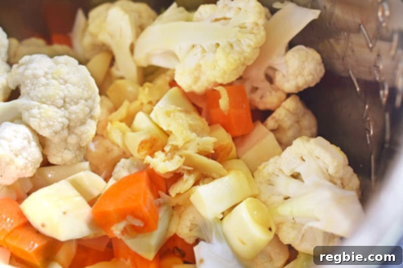 Instant Pot Wholesome Autumn Mash 7 An Instant Pot filled with a colorful medley of chopped parsnips, carrots, and cauliflower, with roasted garlic bulbs nestled among them.