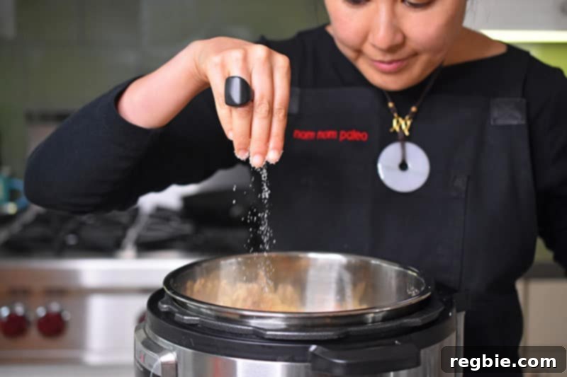 Instant Pot Wholesome Autumn Mash 8 A hand sprinkling Diamond Crystal kosher salt evenly over the vegetables in the Instant Pot, preparing for pressure cooking.
