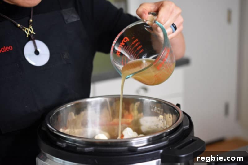 Instant Pot Wholesome Autumn Mash 9 A steady stream of bone broth being poured into the Instant Pot, over the vegetables, ensuring enough liquid for pressure cooking.