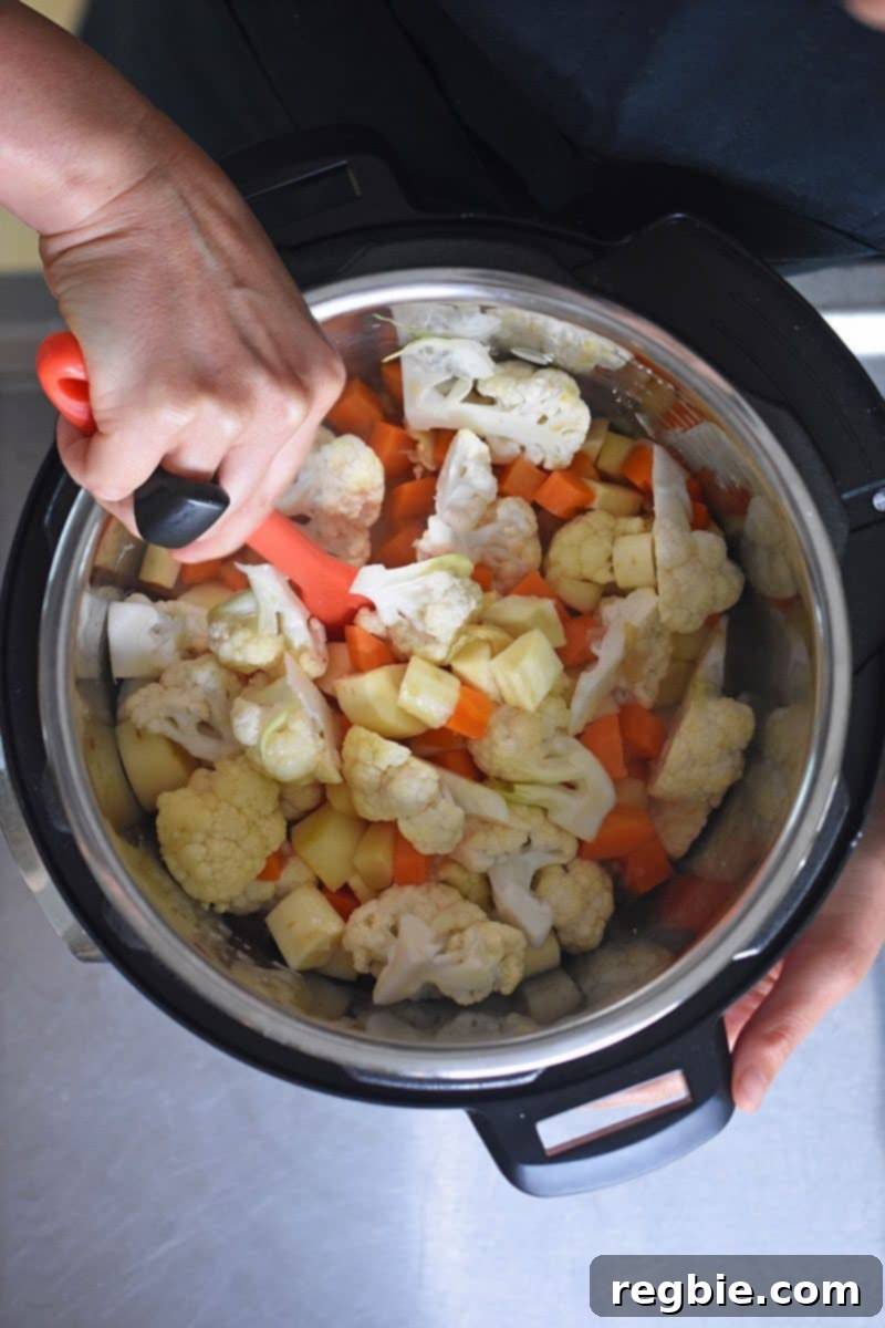 Instant Pot Wholesome Autumn Mash 10 A rubber spatula stirring the colorful mixture of parsnips, carrots, and cauliflower in the Instant Pot, ensuring even distribution of broth and salt.