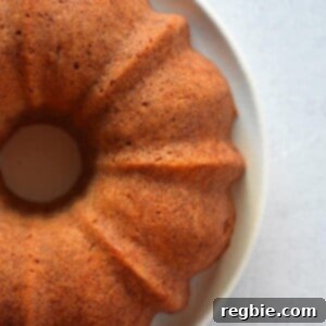 An elegant overhead shot of three-quarters of a golden-brown apple Bundt Cake resting on a pristine white plate, promising a delicious, comforting dessert.