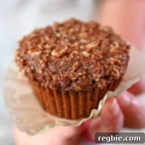 A hand gently holds a freshly baked paleo and gluten-free apple muffin, its paper liner delicately unwrapped, revealing a moist and inviting texture.