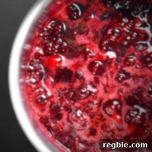 An inviting overhead shot of paleo cranberry sauce, richly red and simmering gently in a saucepan, hinting at its addictive sweet and tangy flavor.