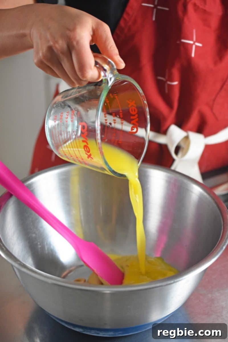 Someone pouring orange juice into a metal bowl to make paleo and Whole30 Orange Dijon Chicken