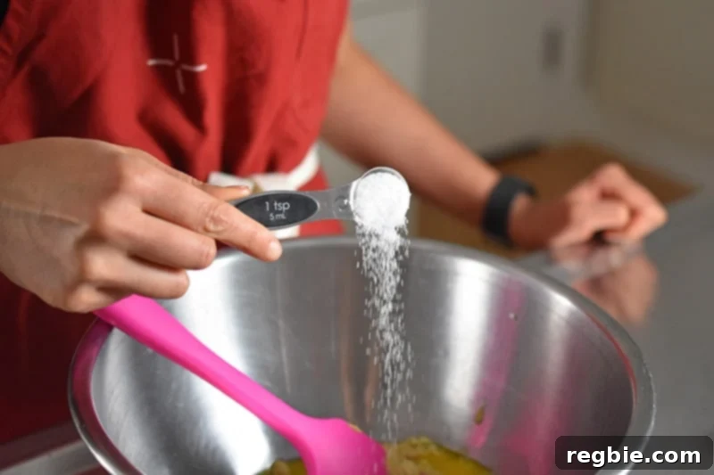 Someone adding salt into a metal bowl for the orange dijon chicken marinade.