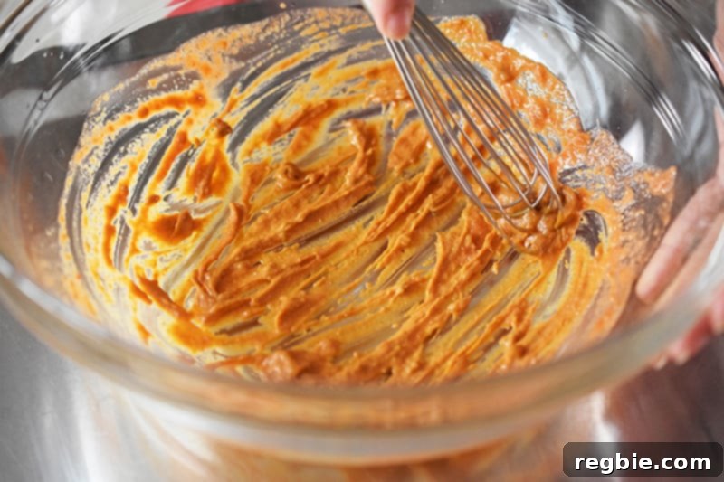 A close-up shot of a whisk blending the spicy Thai sauce in a bowl, showcasing its creamy, uniform consistency.