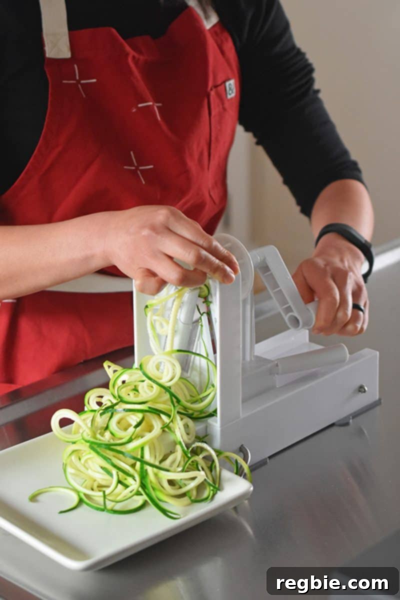 A person actively spiralizing a fresh zucchini over a bowl, demonstrating the creation of long, curly zoodles.