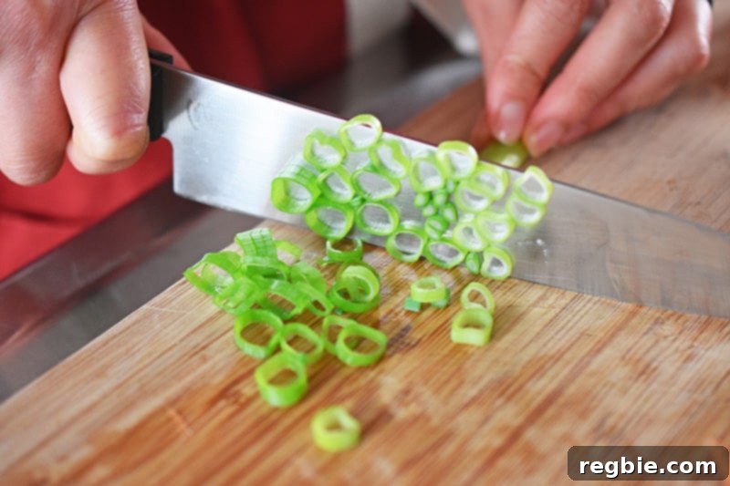A hand expertly chopping fresh green onions on a cutting board, preparing them for the spicy Thai zoodle salad.