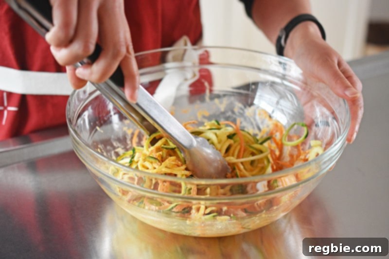 A vibrant mix of julienned vegetables and shredded chicken being tossed vigorously with the spicy Thai marinade in a large bowl, ensuring even coating.