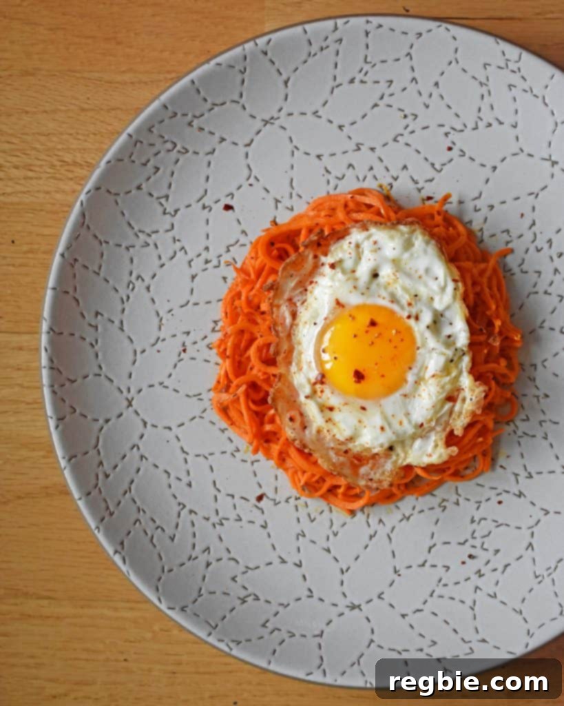 An overhead shot of Sweet Potato Hash with Fried Eggs on a white plate, garnished with a sprinkle of Aleppo pepper.