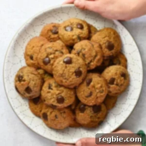 An overhead shot of two hands holding a white plate piled high with paleo banana chocolate chip cookies, a perfect wholesome gift.