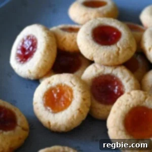A blue plate is piled high with paleo and gluten free thumbprint cookies, some filled with apricot and others with strawberry jam.