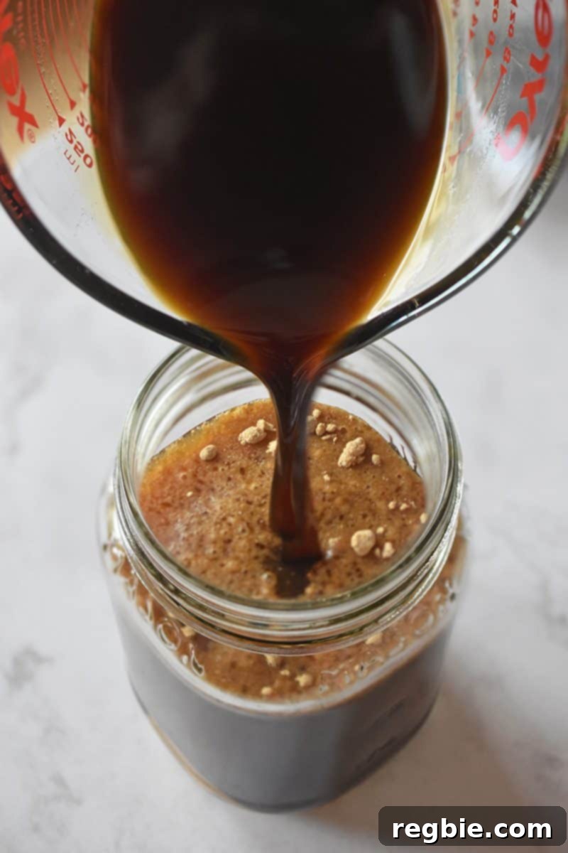 Pouring the first ingredients of the All-Purpose Stir-Fry Sauce into a mason jar, demonstrating the simple mixing process.