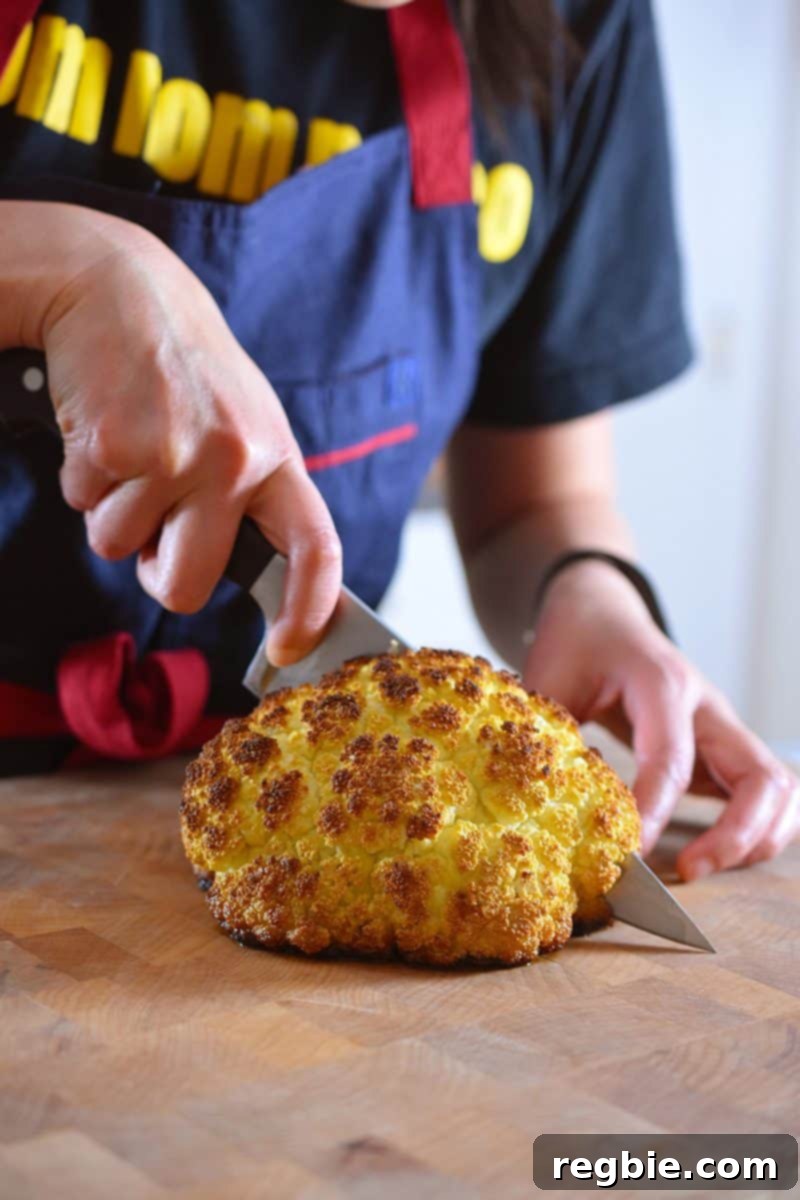 Whole Roasted Cauliflower being sliced with a chef's knife on a cutting board, ready to be served.