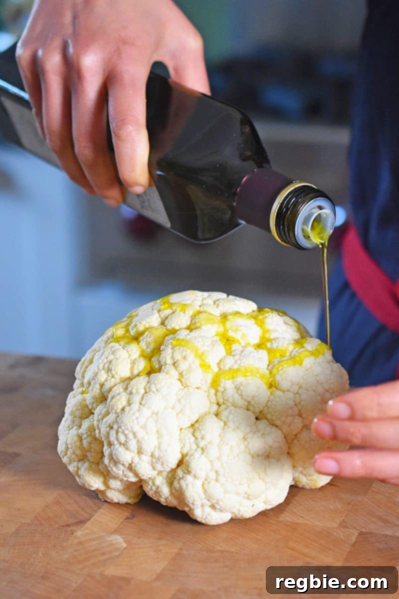 A stream of olive oil being poured on top of a small cauliflower head, ready for seasoning.