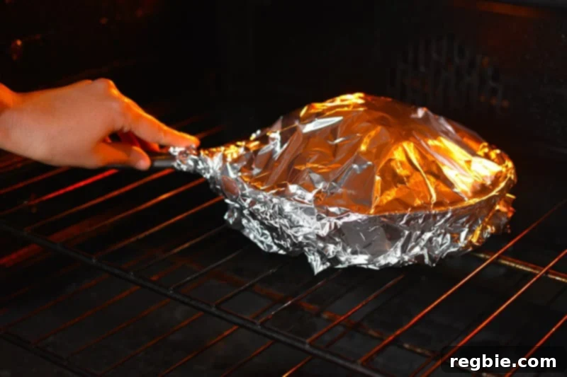 The foil-covered cast iron skillet with the seasoned cauliflower head is placed in the oven to begin cooking.