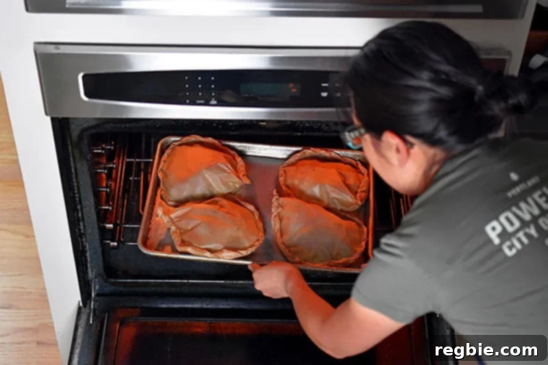 Someone placing a tray of four packs of the paleo paper-wrapped chicken into the oven.