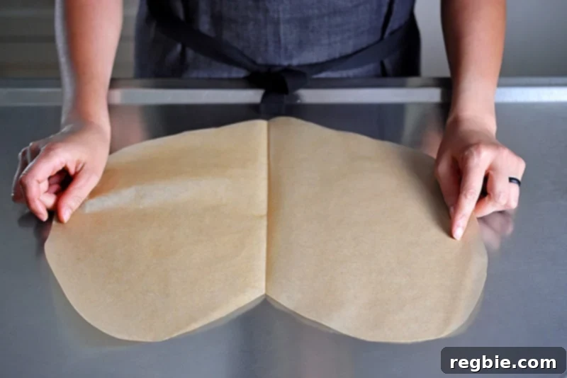 Someone laying flat the heart-shaped parchment paper on a countertop for the paper-wrapped chicken recipe.
