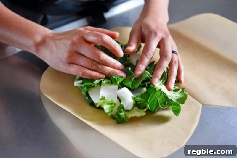 Someone assembling chopped and seasoned bok choy on the heart-shaped parchment paper for paper-wrapped chicken.