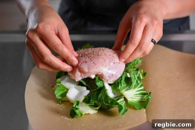 Someone placing the raw and seasoned chicken on top of the bok choy for the paper-wrapped chicken recipe.
