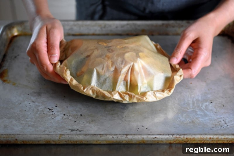 Someone placing the parchment paper packet on an aluminum baking sheet.