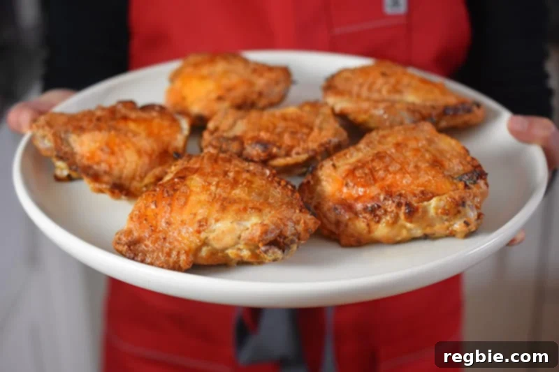 Umami-Rich Roasted Chicken Whole30 Keto 4 A person presenting a perfectly roasted Umami Roast Chicken thigh on a small plate, showcasing its crispy skin and tender meat.