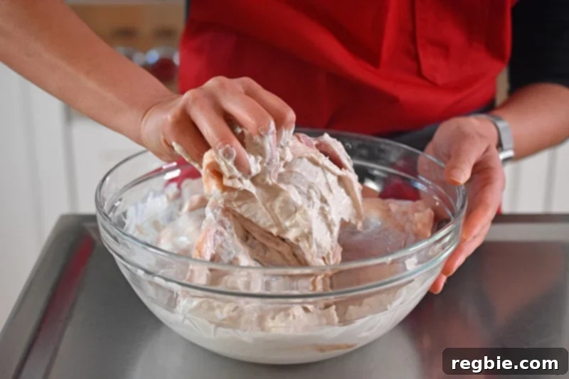 Umami-Rich Roasted Chicken Whole30 Keto 7 Someone using their hands to thoroughly combine bone-in, skin-on chicken thighs with the creamy marinade for Umami Roast Chicken in a large bowl.