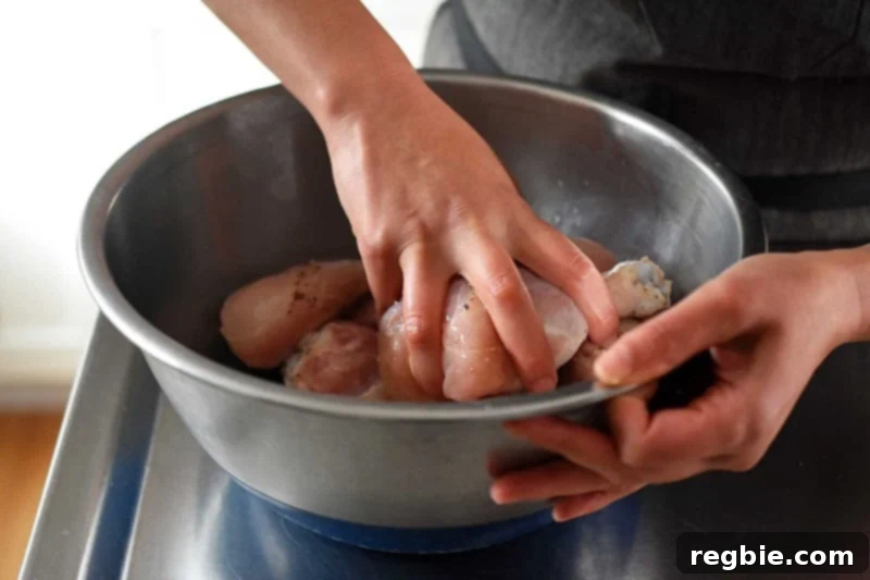 Someone skillfully tossing the seasoned chicken for the lemongrass and coconut stew in a shiny metal bowl.