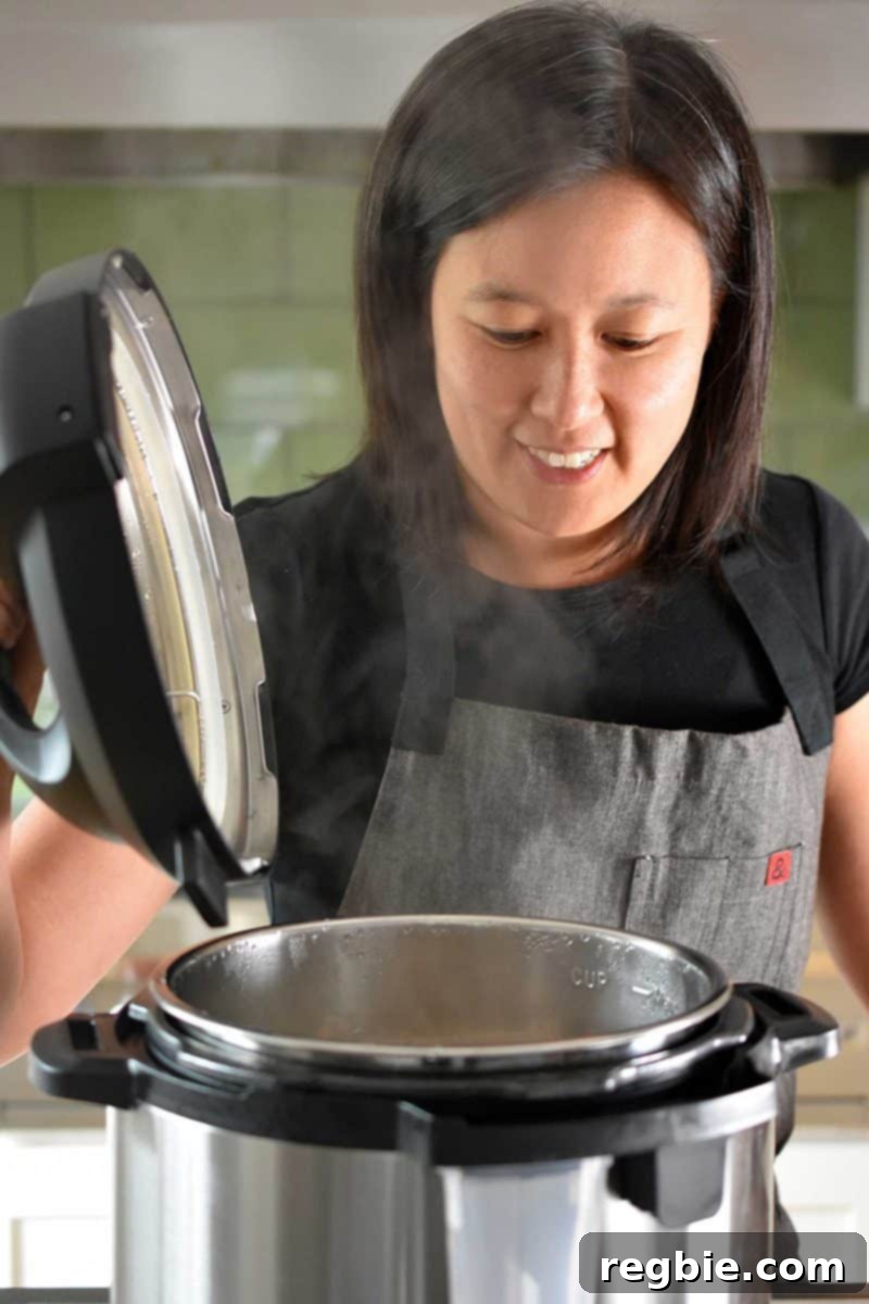 Creamy Instant Pot Lemongrass Coconut Chicken 17 A woman opening up an Instant Pot, revealing the cooked lemongrass and coconut chicken stew inside, ready for final seasoning.