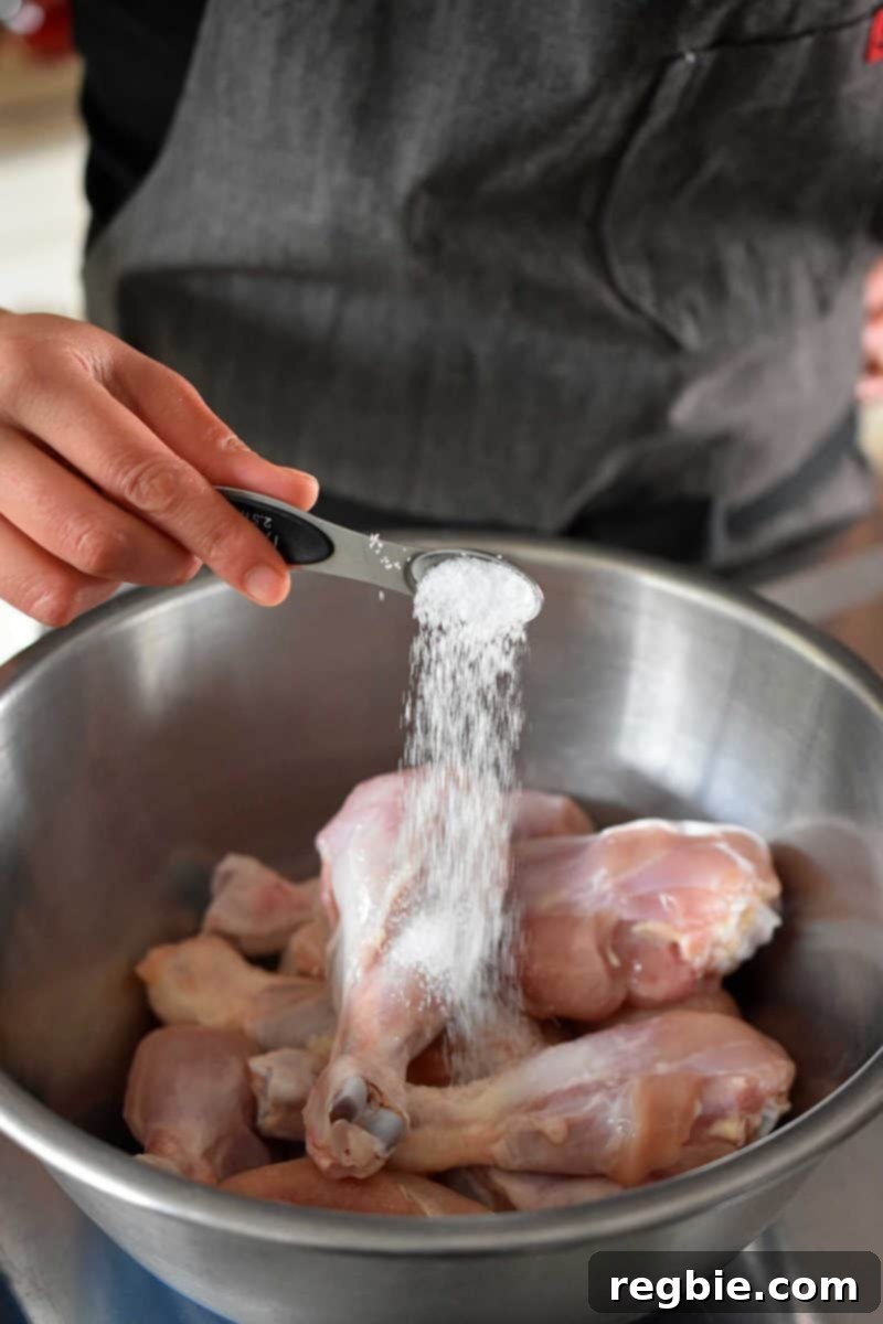 Creamy Instant Pot Lemongrass Coconut Chicken 10 Someone adding a liberal amount of salt to raw chicken drumsticks in a metal bowl, seasoning them perfectly.