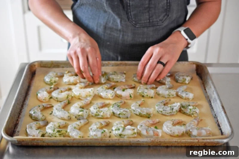Someone meticulously placing the marinated shrimp in neat rows on a parchment-lined baking sheet, ready for roasting.