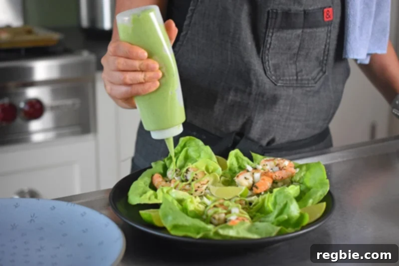 Someone is squeezing a bottle filled with delicious paleo and dairy-free avocado crema on top of the assembled paleo shrimp tacos, adding a final touch of flavor.