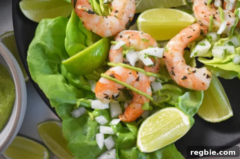 An inviting overhead shot of delicious paleo shrimp tacos, nestled on butter lettuce leaves, garnished with fresh cilantro, onions, and bright lime wedges.