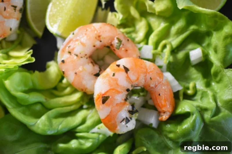 A close-up of two perfectly cooked shrimp resting on a crisp lettuce leaf, accompanied by a fresh lime slice.