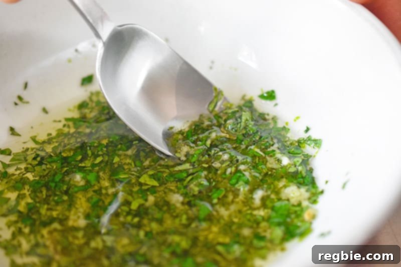 In a small bowl, someone is stirring the vibrant marinade for the paleo shrimp tacos, featuring oil, oregano, garlic, and lime zest.